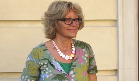 Das Portraitbild von Karin Sommer zeigt eine blonde Frau mit dunkler Brille und grün gemustertem Kleid.