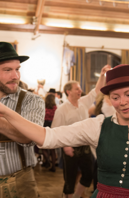 - Mitten auf einer vollen Tanzfläche führt ein Tänzer in Tracht seine Partnerin um sich herum.
