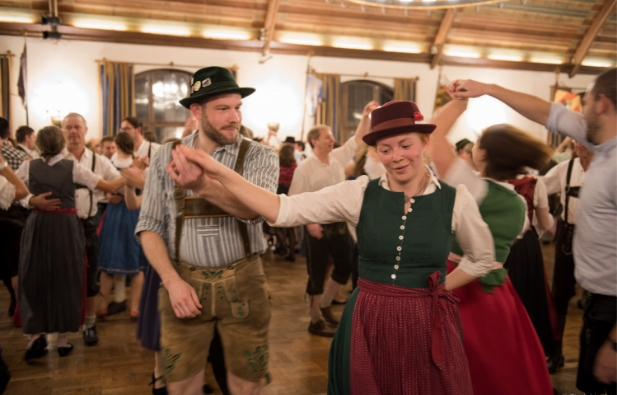 - Mitten auf einer vollen Tanzfläche führt ein Tänzer in Tracht seine Partnerin um sich herum.