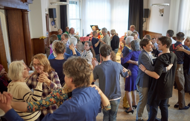 - Viele Tanzpaare unterschiedlichen Alters tanzen in einem kleinen Saal zu Live Musik.