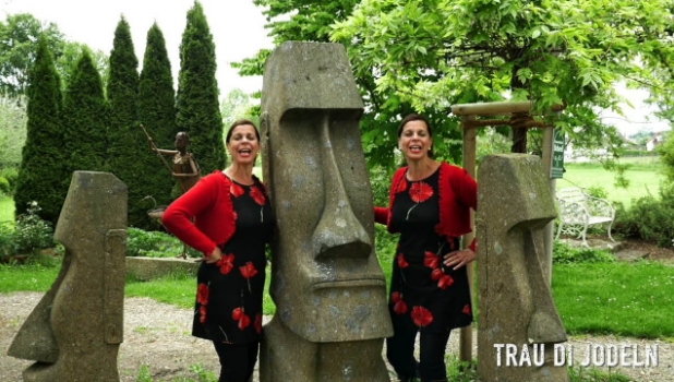 An einer steinernen Statue stehen zwei bunt gekleidete Frauen und singen.