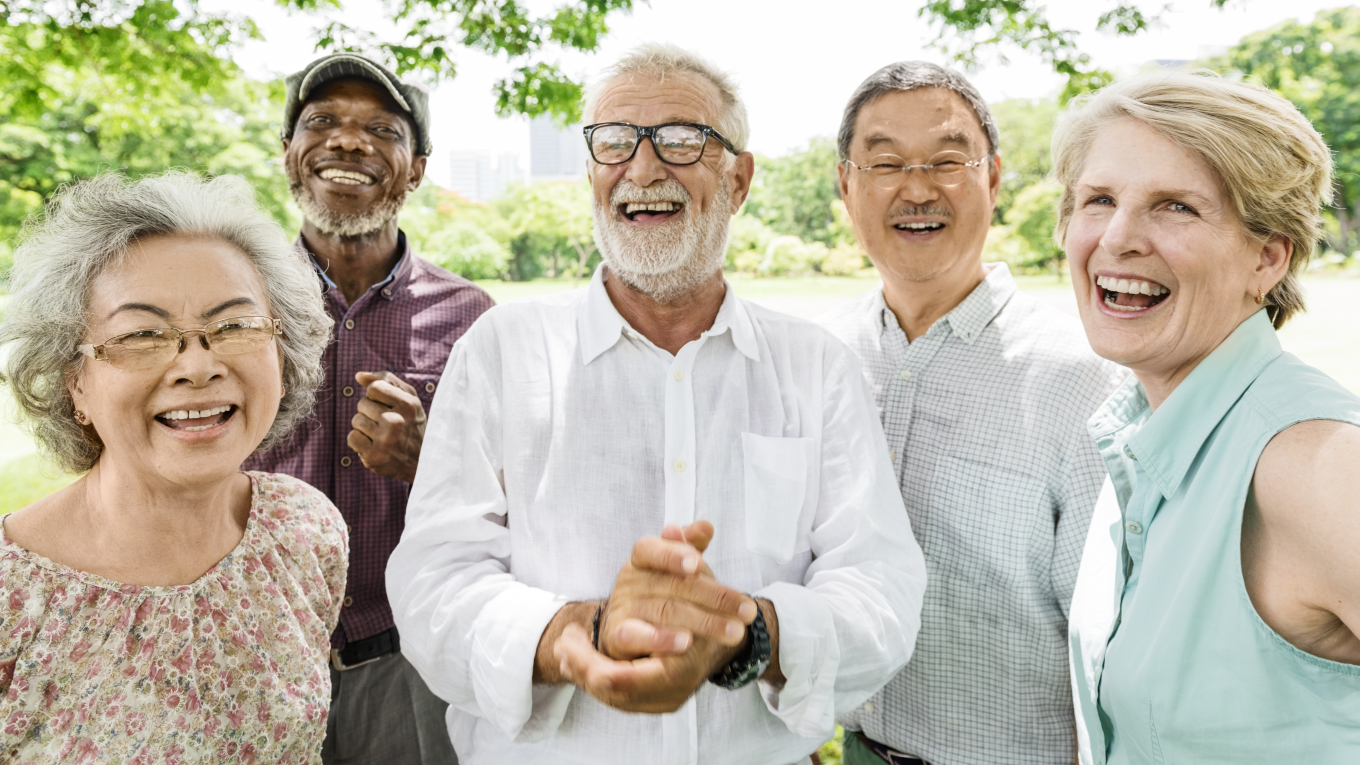 eine Gruppe von älteren Menschen steht lachend im Grünen