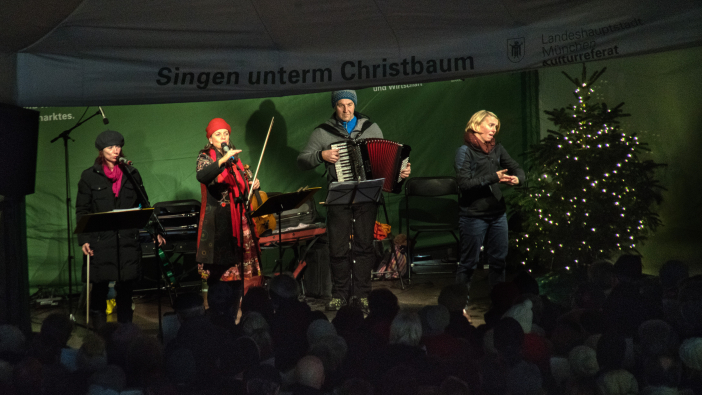 Drei Musiker*innen und eine Gebärdensprachdolmetscherin stehen auf der Bühne und musizieren Weihnachtslieder