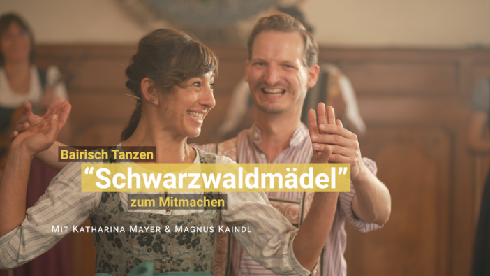 Eine Tänzerin im Dirndl und ein Tänzer in Lederhosen lächeln in Tanzhaltung in die Kamera.