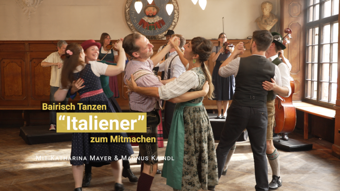 Vier Tanzpaare im bayerischer Kleidung wiegen miteinander hin und her. Im Hintergrund spielt Livemusik.