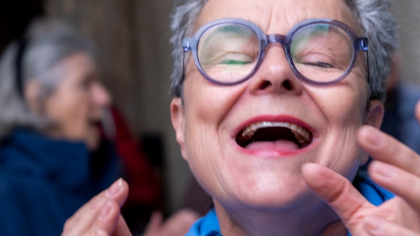 Dame mit weisser Kurhaarfrisur und markanter Brille singt konzentriert mit geschlossenen Augen