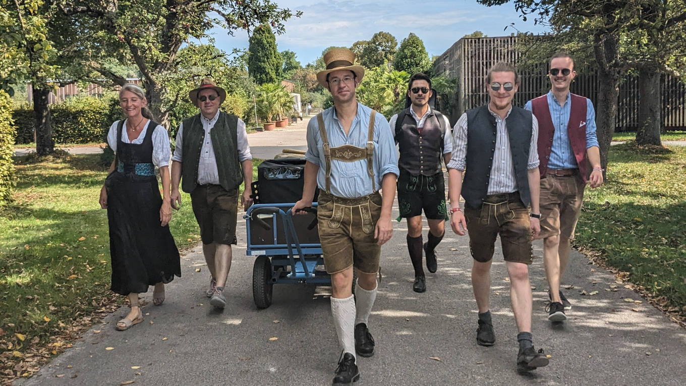 Eine Gruppe Musiker geht auf einem Weg und zieht einen Rollwagen voller Instrumente.