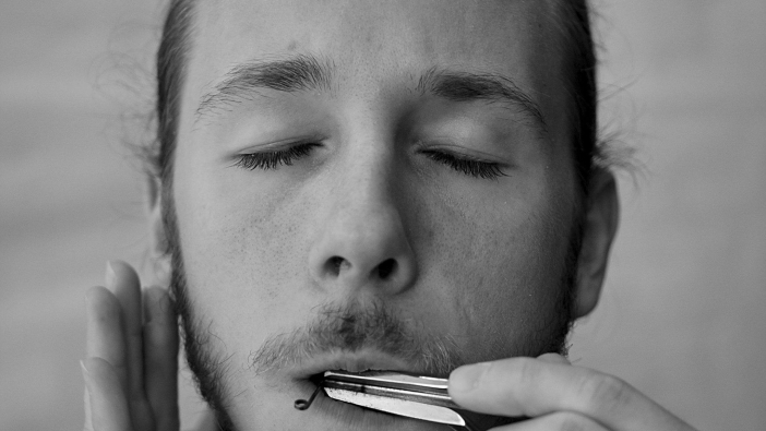 Junger Mann mit geschlossenen Augen und Maltrommel im Mund