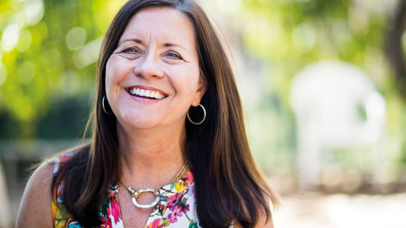 Eine Frau mittleren Alters und langen Haaren lächelt in die Kamera